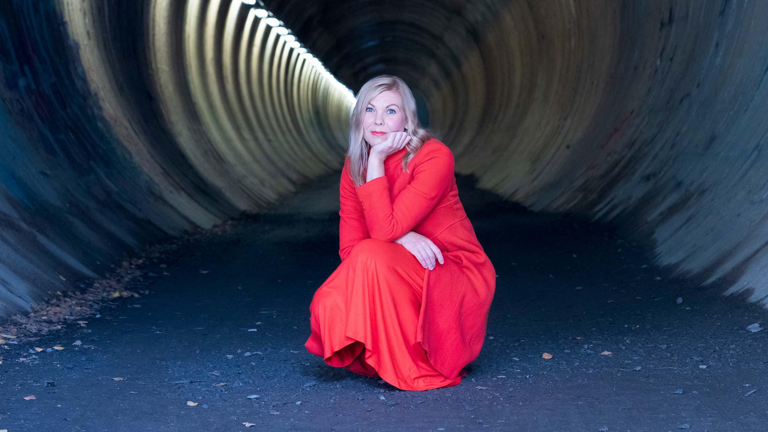 Minna Leinonen kyykyssä tunnelissa punainen mekko päällään.